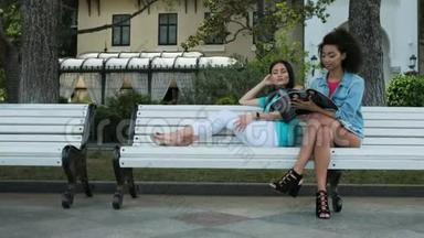 两个女孩<strong>坐在公园里</strong>聊天，看杂志
